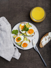 Toast with cream cheese, avocado and eggs on plate at wooden background