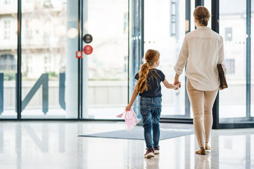 A rear view of businesswoman with small daughter walking in office building.