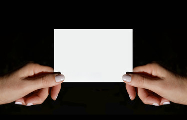 Tarjeta blanca para escribir texto con manos de mujer sobre fondo negro, aisladas.
