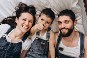 Happy family making selfie on bed. Lokk at camera and show with finger on it. Parents spending free time with their son.