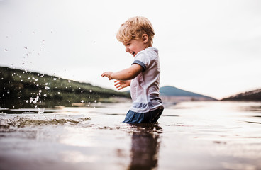 A wet, small toddler boy standing outdoors in a river in summer, playing. © Halfpoint