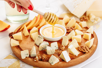 Woman Hand Pouring Honey to Cheese Board Gourmet Side View. Girl Taste French Cheeseboard with Brie, Parmesan and Mozzarella Assorted. Gouda and Walnut Various Dessert Platter