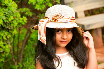 Small Indian girl wearing round fancy cap looking at camera, Pune.