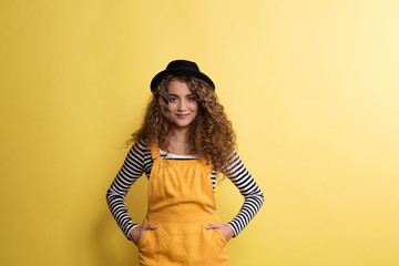 Portrait of a young woman with black hat in a studio on a yellow background.