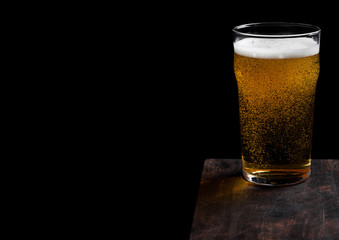 Glass of lager beer with foam and bubbles on vintage wooden board on black background. Space for text