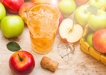 Glass of homemade organic apple cider with fresh apples in bamboo basket on wooden background