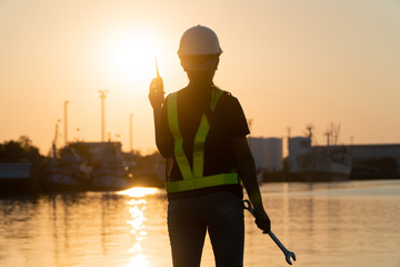 Silhouettes of asian woman engineer holding wrenches and radio communication (walkie talkie) she...
