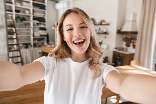 Image closeup of content blond woman looking at camera and taking selfie photo in living room