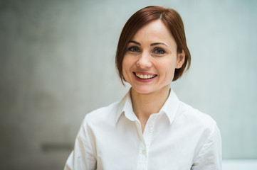 A portrait of young businesswoman standing in office, looking at camera.