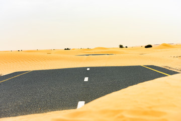 (Selective focus) Stunning view of a deserted road covered by sand dunes. Empty road that run...