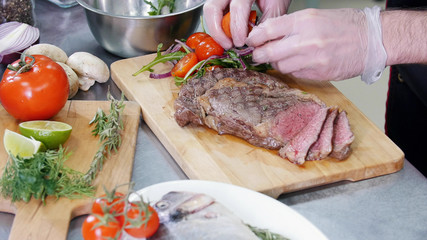 A chef working in the kitchen. A man serving the steak with vegetables