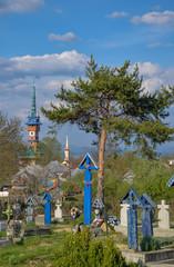 Fototapeta na wymiar Wooden tombs on Merry Cemetery and traditional maramures neo-gothic church in Sapanta village, Romania