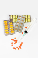 multi-colored yellow orange brown pills and medical syringe on a white background