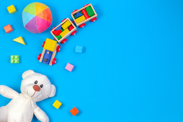 Baby kids toys background. White teddy bear, wooden train, colorful blocks on blue background