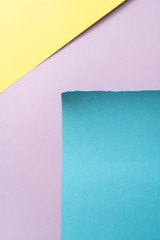 Vertical yellow-blue-purple geomethric  paper background. A piece of blue paper in the down-right corner with torn edges, and yellow triangle in the up-left corner of purple background 