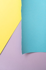 Vertical yellow-blue-purple geomethric  paper background. A piece of blue paper in the up-right corner with torn edges 