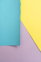 Vertical yellow-blue-purple geomethric  paper background. A piece of blue paper in the up-left corner with torn edges 