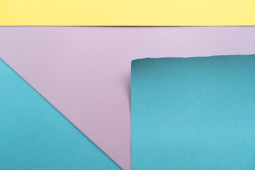 Purple-blue-yellow paper background. A piece of blue paper with torn edges, yellow stripe and blue triangle on the background of a sheet of purple paper