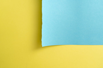 Yellow-blue paper background. A piece of blue paper in the up-right corner with torn edges on the background of a sheet of yellow paper