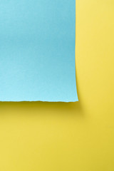 Vertical yellow-blue paper background. A piece of blue paper in the up-left corner with torn edges on the background of a sheet of yellow paper