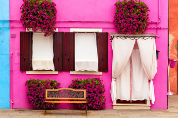 Fototapeta na wymiar Pink house with pink flowers and plants. Nice bench under windows. Colorful house in Burano island near Venice, Italy