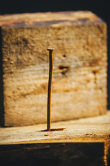 Old long rusty curve nail hammered into a wooden bar on a rustic wooden background close-up. macro