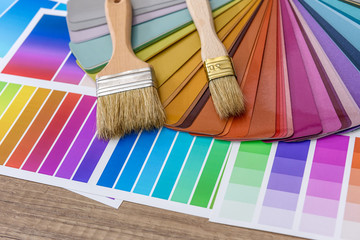 Brushes and paint color palette samples on wooden background, closeup