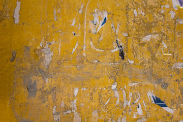 old dirty yellow concrete wall with damages, gray stains of paint and remnants of torn paper ads....