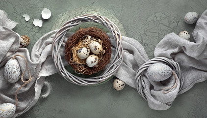 Easter flat lay on dark background with quail eggs in the nest, linen fabrique and two golden eggs on dark