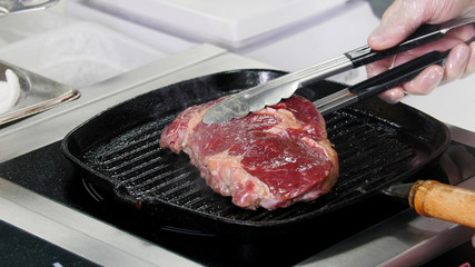 Working in the kitchen. Chef starts frying raw piece of steak in the pan