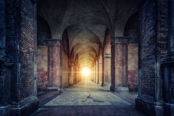 Rays of divine light illuminate old arches and columns of ancient buildings. Bologna, Italy....