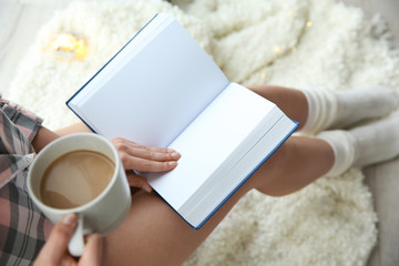 Young woman with cup of coffee reading book at home, above view