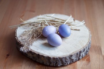 Easter lilac eggs with wheat branches on wooden stand close-up blurred background