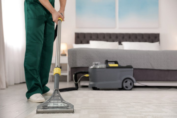 Professional janitor removing dirt from carpet with vacuum cleaner in bedroom, closeup. Space for...