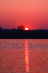 Naklejka premium Wonderful and romantic sunrise. Half of rising sun on the horizon with its golden reflections in the water