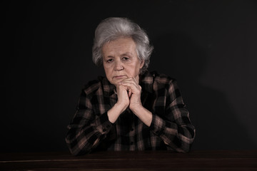 Poor upset woman sitting at table on dark background