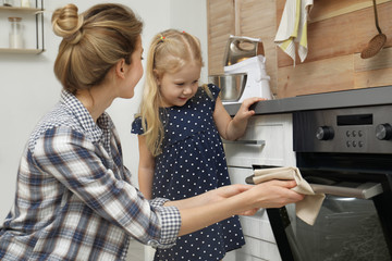 Mother and her daughter baking food in oven at home