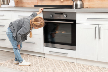 Little girl waiting for preparation of cookies in oven at home
