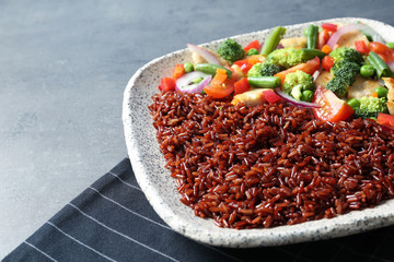 Plate with cooked brown rice on table, closeup. Space for text