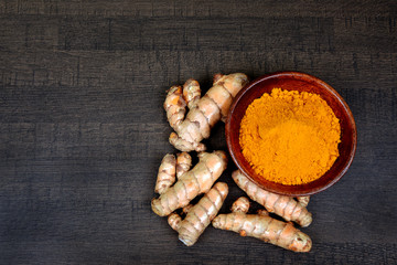 Organic healthy Turmeric powder in a bowl with Turmeric roots on wooden background