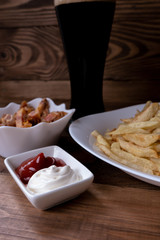 Vertical. Close-up of snacks and sauses to dark beer on a dark wooden background. Men's set to watch a football match