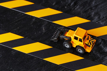 Naklejka premium Yellow toy bulldozer on a black background texture. Black and yellow fence tape against the background of the CONCEPT