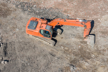 Orange excavator on caterpillars in the foundation pit during the construction of the building...