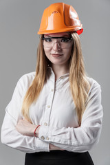 Portrait of a young attractive woman with blond hair in orange helmet on a neutral gray background.