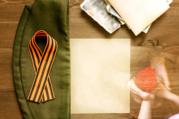 St. George ribbon, soldier's cap, photos on a paper background / St. George ribbon-a symbol of the great Victory / victory Day. Hands of a child and a veteran with a red carnation.