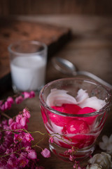 Thapthim krop, mock pomegranate seeds in coconut and syrup in the glass on the wood table there are flower, spoon and coconut milk placed around.