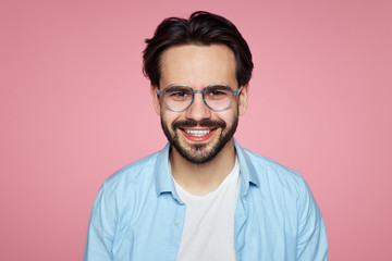 Attractive hipster male smiling at camera, glad to find suitable well paid job, isolated over pink background.