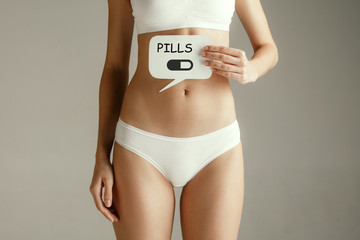 Woman health. Female model holding card with word PILLS near stomach. Young adult girl with paper...