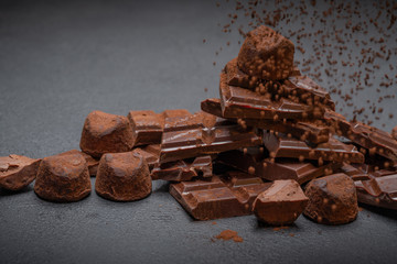 Dark or milk organic chocolate pieces, cocoa powder and truffle candies on dark concrete backgound