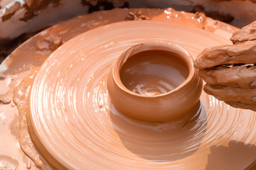 Hands of a street potter make a clay pot on a potter's wheel. Close-up